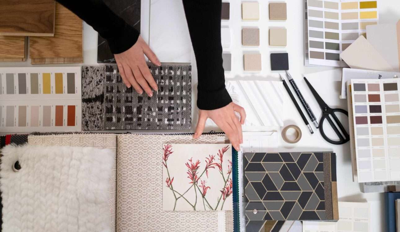 Luxury interior design workspace with floor plans, calculator, color swatches, material samples, and a modern living room representing interior designer pricing and renovation planning.