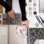 Luxury interior design workspace with floor plans, calculator, color swatches, material samples, and a modern living room representing interior designer pricing and renovation planning.